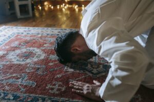 Man in White Thobe Bowing Down on Red and Blue Rug