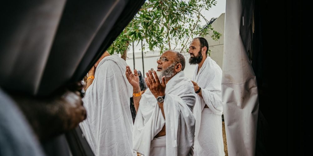 A group of men in white robes participate in a spiritual prayer outdoors, embracing cultural and religious traditions.