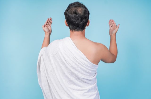 Back portrait of young Asian Muslim man wearing ihram praying with hand gesture. Hajj concept.