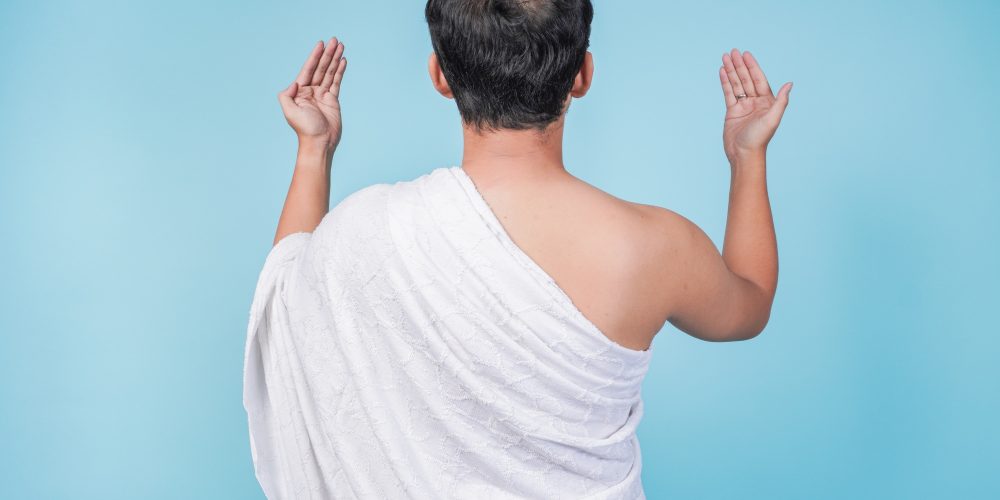 Back portrait of young Asian Muslim man wearing ihram praying with hand gesture. Hajj concept.